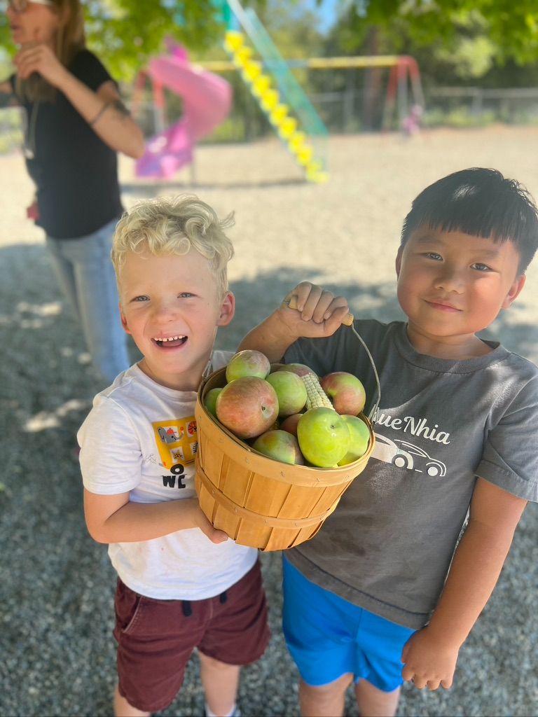 two young children holding a bucket of apples